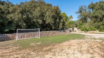 A soccer goal in a grassy area with a stone wall and trees in the background.