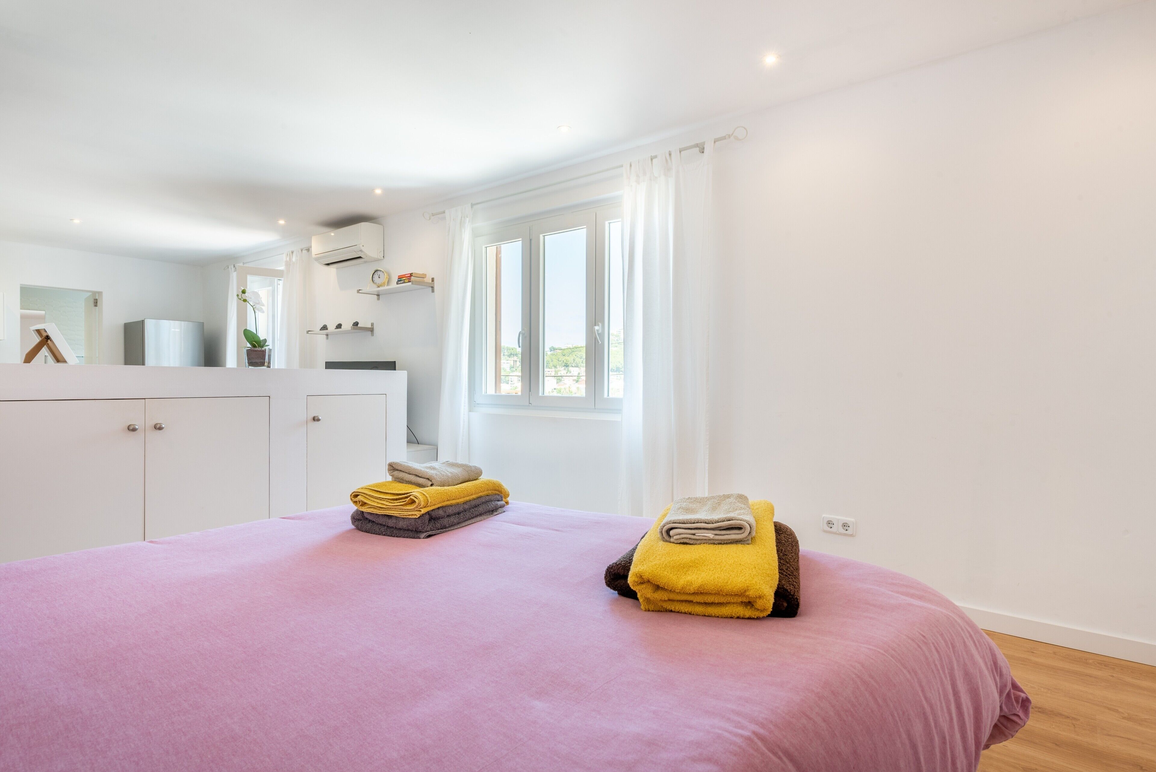 Een slaapkamer met een bed, een kledingkast, een raam met gordijnen en een kleine kitchenette.