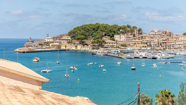 Un pueblo costero con un puerto deportivo, edificios y una colina con árboles.