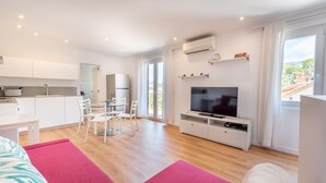 Una habitación moderna y luminosa con comedor, televisor y un amplio ventanal.