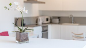 Una orquídea en maceta sobre una mesa blanca en una cocina moderna con armarios blancos y un microondas.