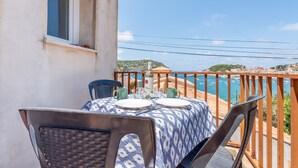 Un balcón con una mesa preparada para dos, con vistas a la costa y barandilla de madera.