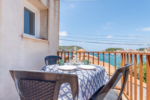 A balcony with a table set for two, overlooking a coastal area with a wooden railing.