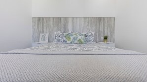 Een bed met een beddegoed met een patroon, een hoofdbord met een getextureerd ontwerp en een kleine potplant op het nachtkastje.