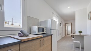 Een moderne keuken met een magnetron, koelkast, houten keukenkastjes en een raam.