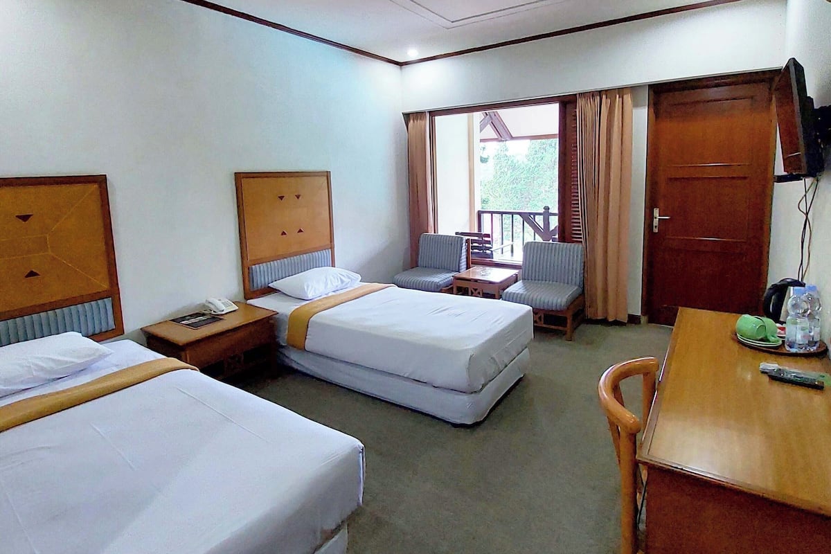 A hotel room with two beds, a desk, a chair, a TV, and a window with curtains.