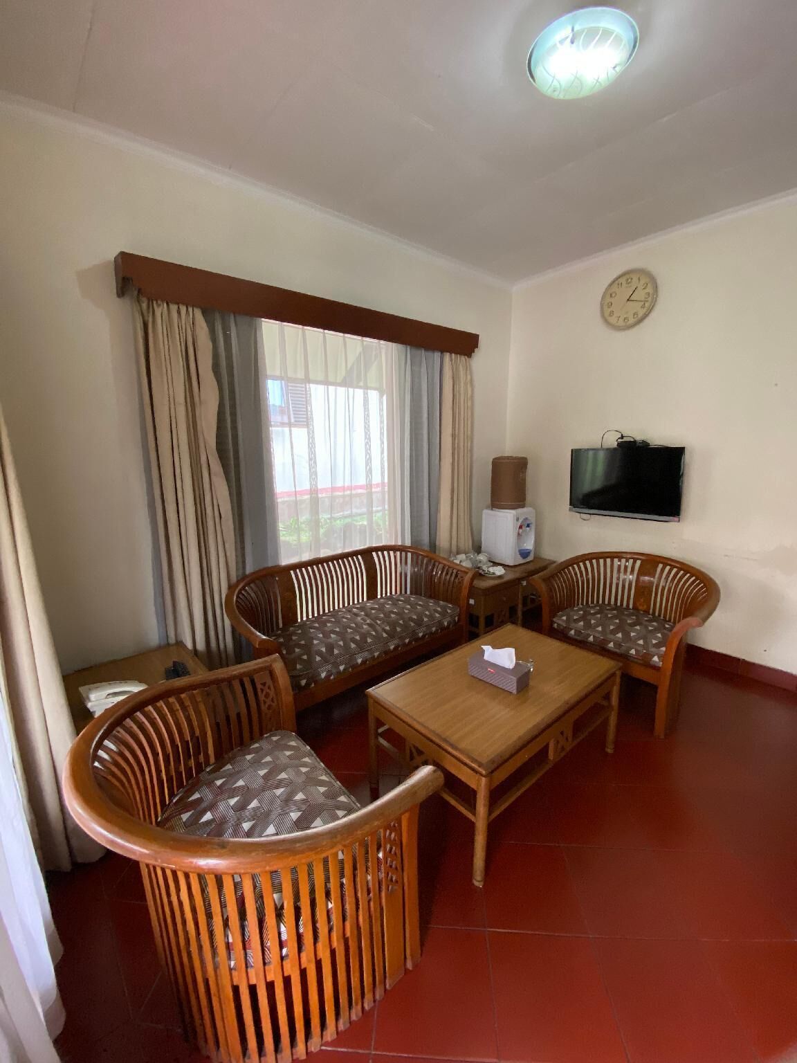 A room with a sofa set, a small table, a television, and a clock on the wall.