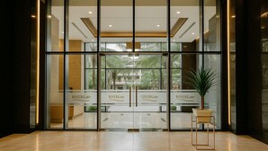 Une entrée d’hôtel moderne avec des portes vitrées, un comptoir d’accueil et une plante en pot.