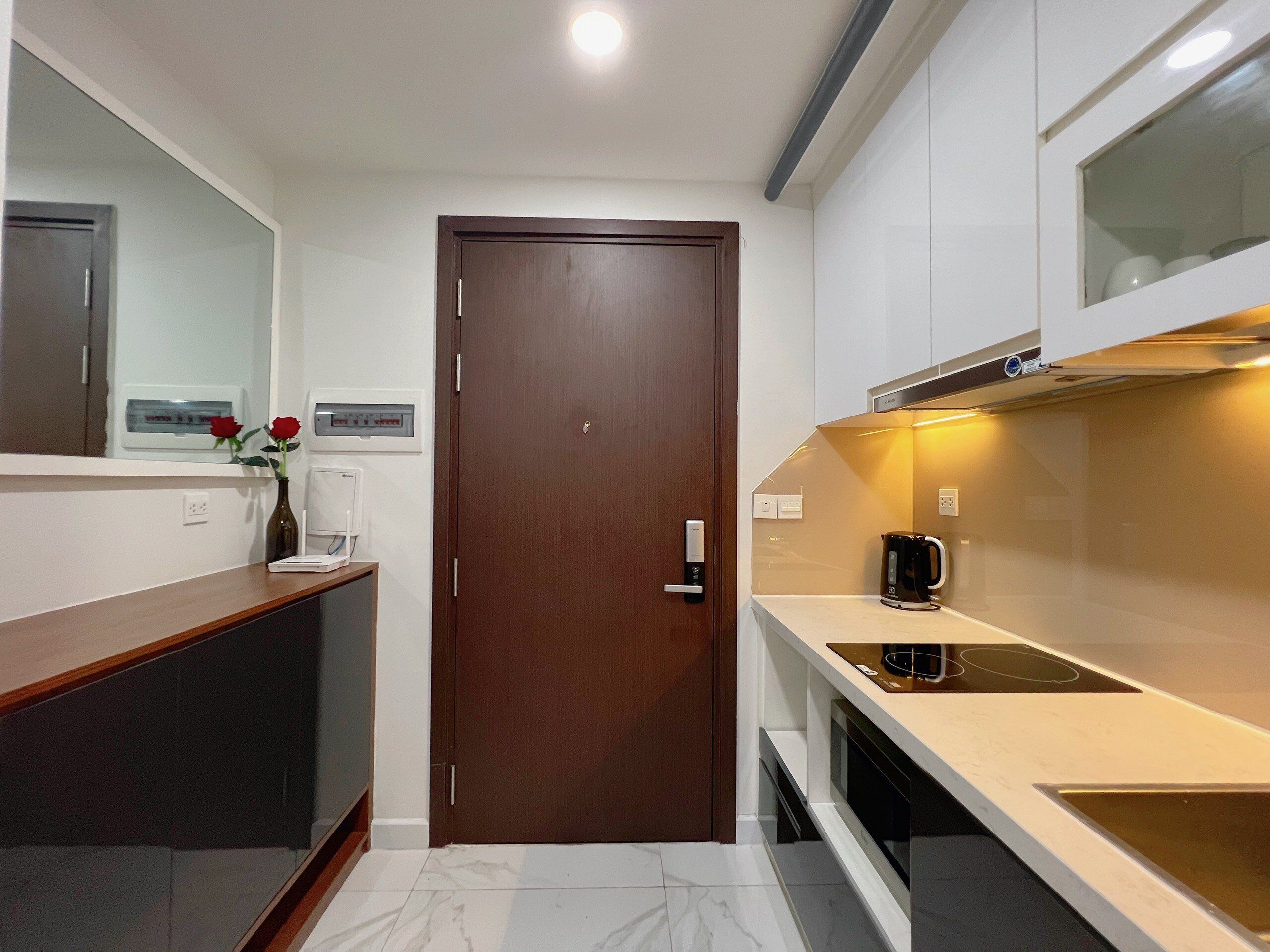 A compact kitchen with a wooden door, white cabinets, a marble countertop, and a coffee maker.