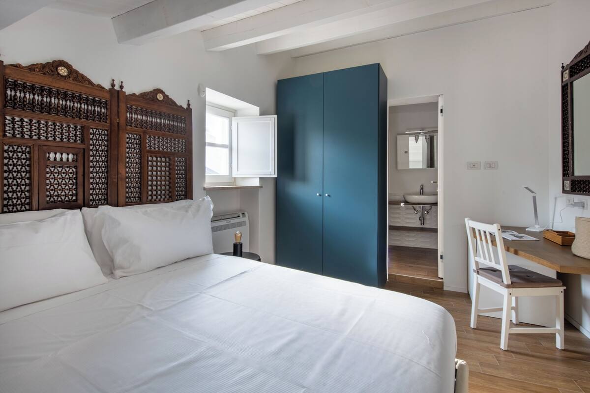 Quarto com cama, cabeceira de madeira, escrivaninha com cadeira e guarda-roupa.