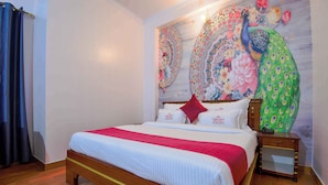 A neatly made bed with a red and white bedspread, a wooden headboard, and a nightstand with a green decorative pillow. - Hotel Parv (Jaipur)