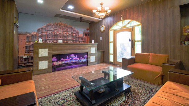 A cozy living room with a glass coffee table, wooden flooring, a fireplace, and a large mural of a historic building. - Hotel Parv (Jaipur)