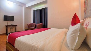 A neatly made bed with a red blanket, a television mounted on the wall, and a chair in the corner. - Hotel Parv (Jaipur)