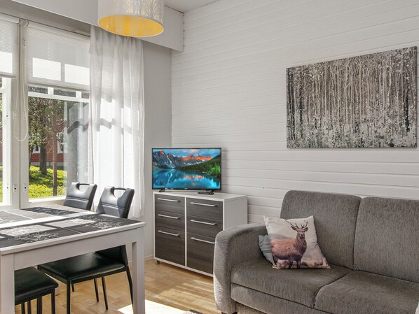 A modern living room with a grey sofa, a television on a cabinet, and a dining area with a table and chairs.