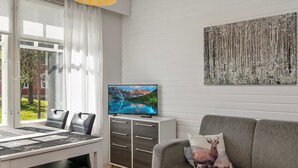 Una sala moderna con comedor, televisor y un ventanal con cortinas.