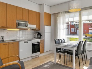 A modern kitchen with wooden cabinets, a microwave, a stove, and a refrigerator. There is a dining area with a table and chairs.