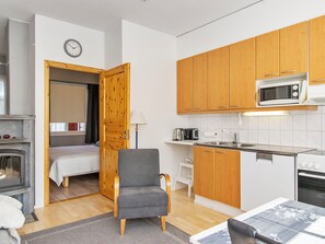 A compact kitchen with wooden cabinets, a microwave, a stove, and a bed in the adjacent room.