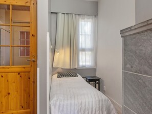 A bedroom with a bed, a nightstand, a window with curtains, and a wooden door.
