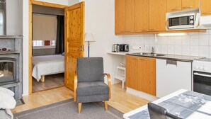 Una habitación de hotel compacta con kitchenette, una cama, una silla y un reloj en la pared.