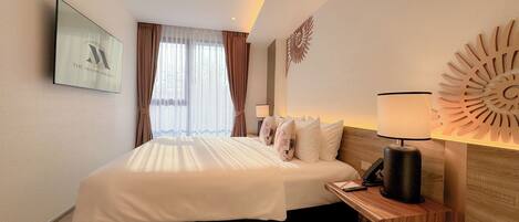 A hotel room with a large bed, a wooden nightstand, a wall-mounted lamp, and a framed picture on the wall.
