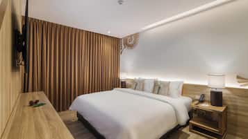 A modern hotel room with a large bed, wooden headboard, a nightstand with a lamp, and a wall-mounted TV.