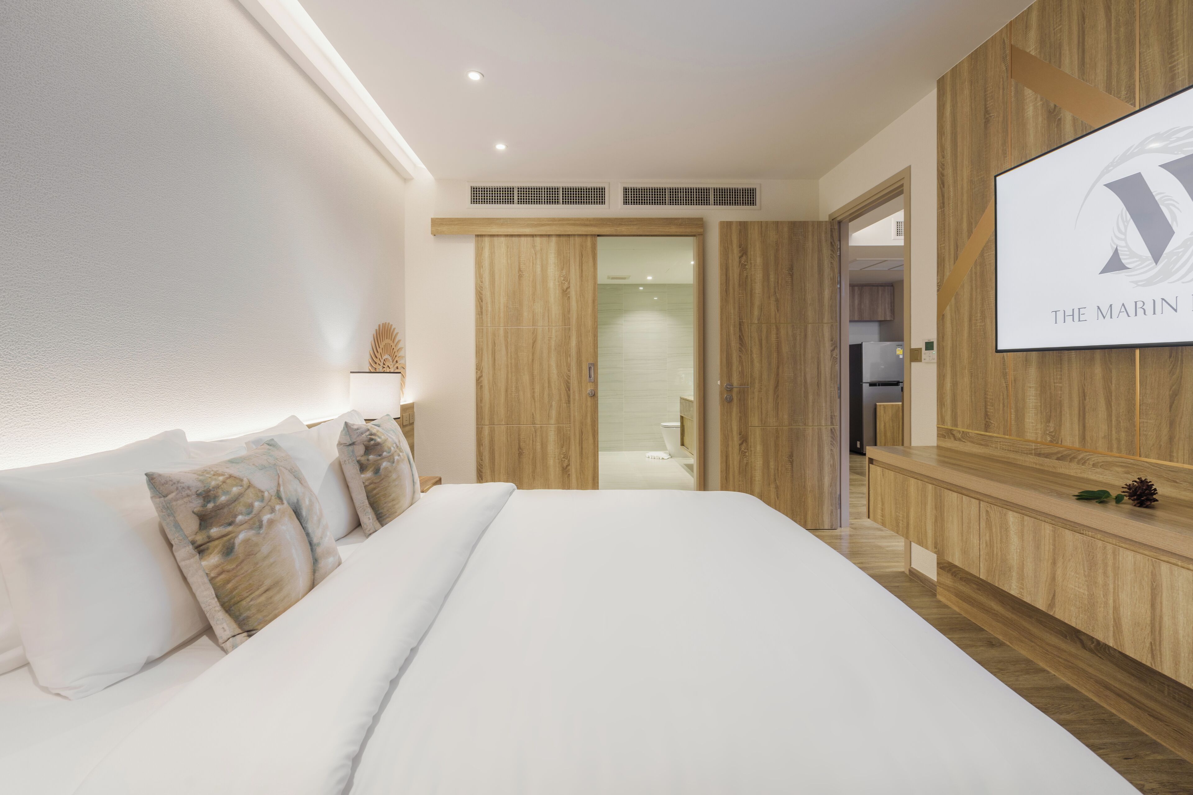 A modern hotel room with a large bed, wooden paneling, a TV screen, and a visible bathroom.