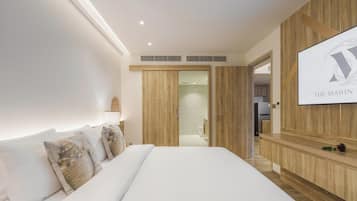Habitación de hotel moderna con una cama grande, paneles de madera, una pantalla de televisión y un baño a la vista.