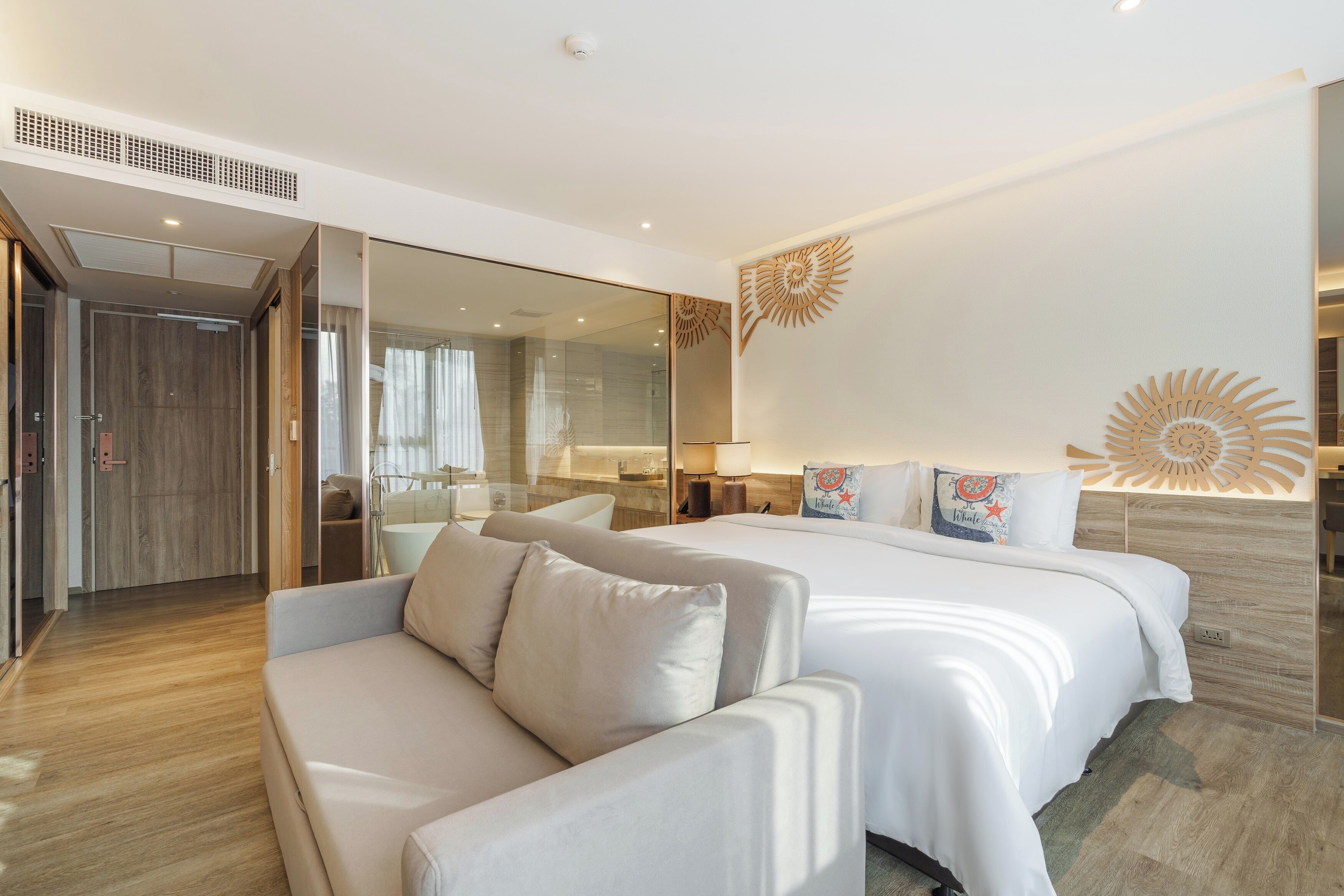 Une chambre d’hôtel moderne dotée d’un grand lit, d’un canapé, d’une cloison en verre et d’un élément décoratif mural.