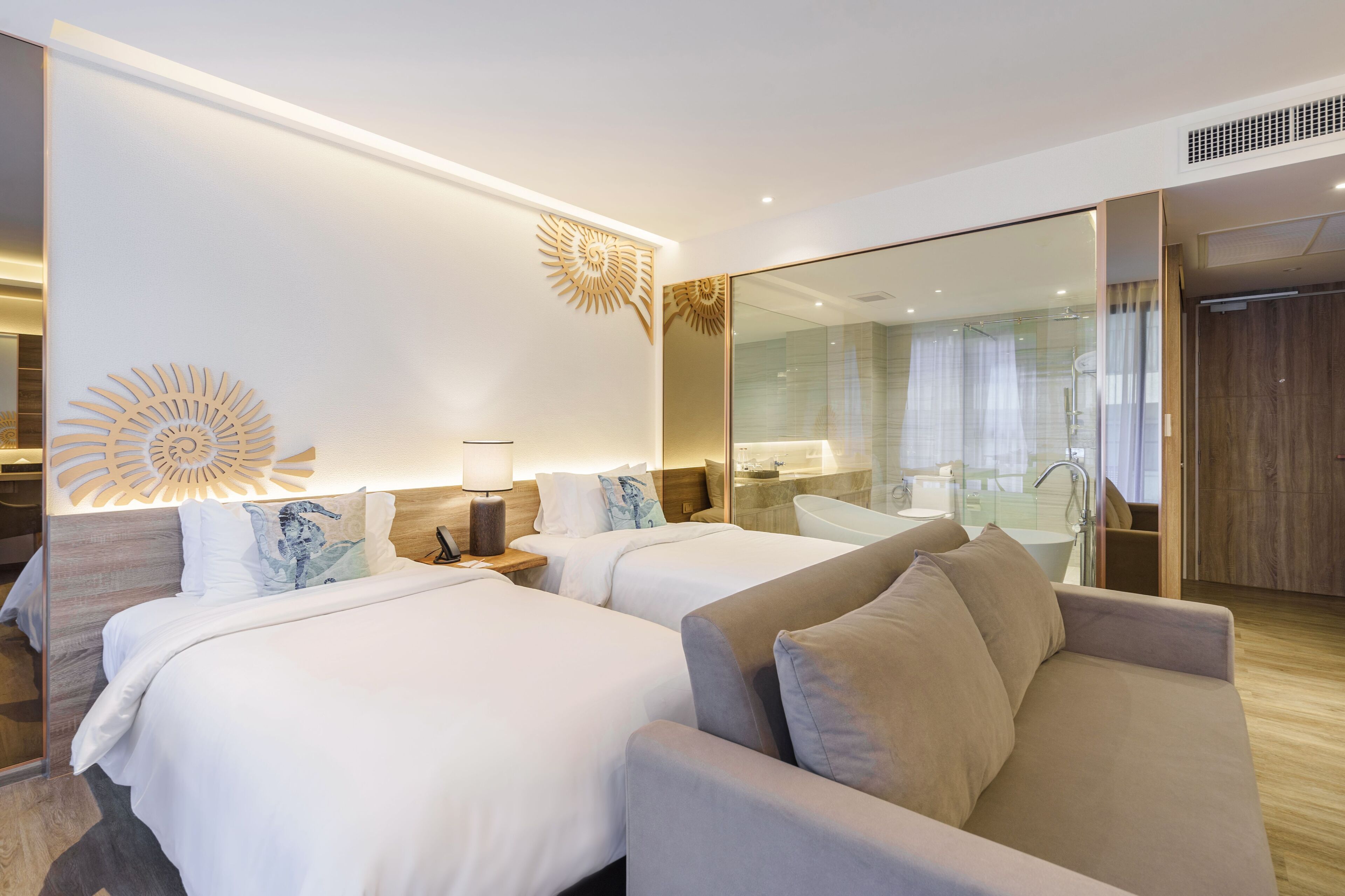 A hotel room with two beds, a sofa, a large mirror, and a glass shower area.