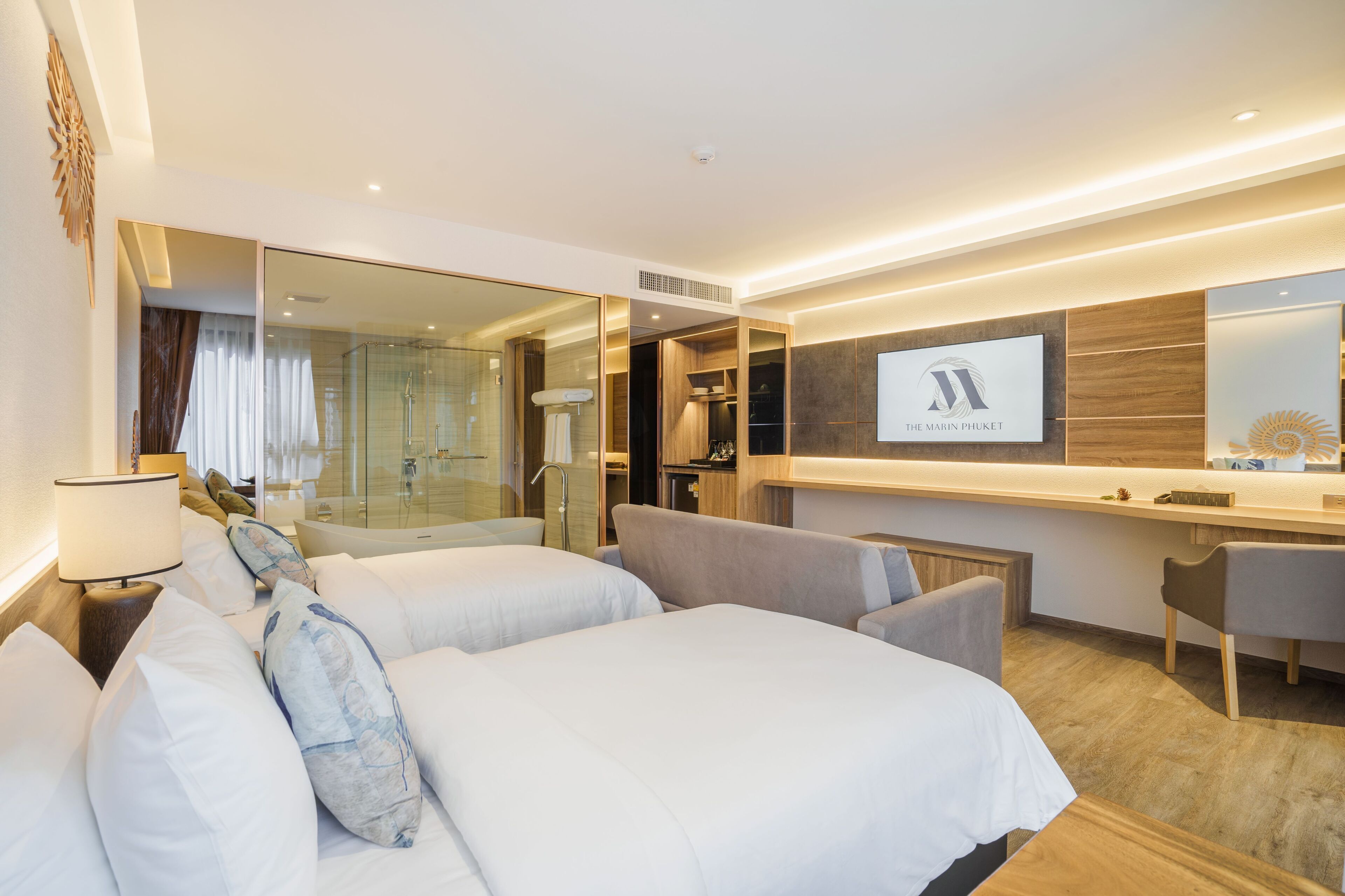 A hotel room with two beds, a desk, a mirror, and a shower area.