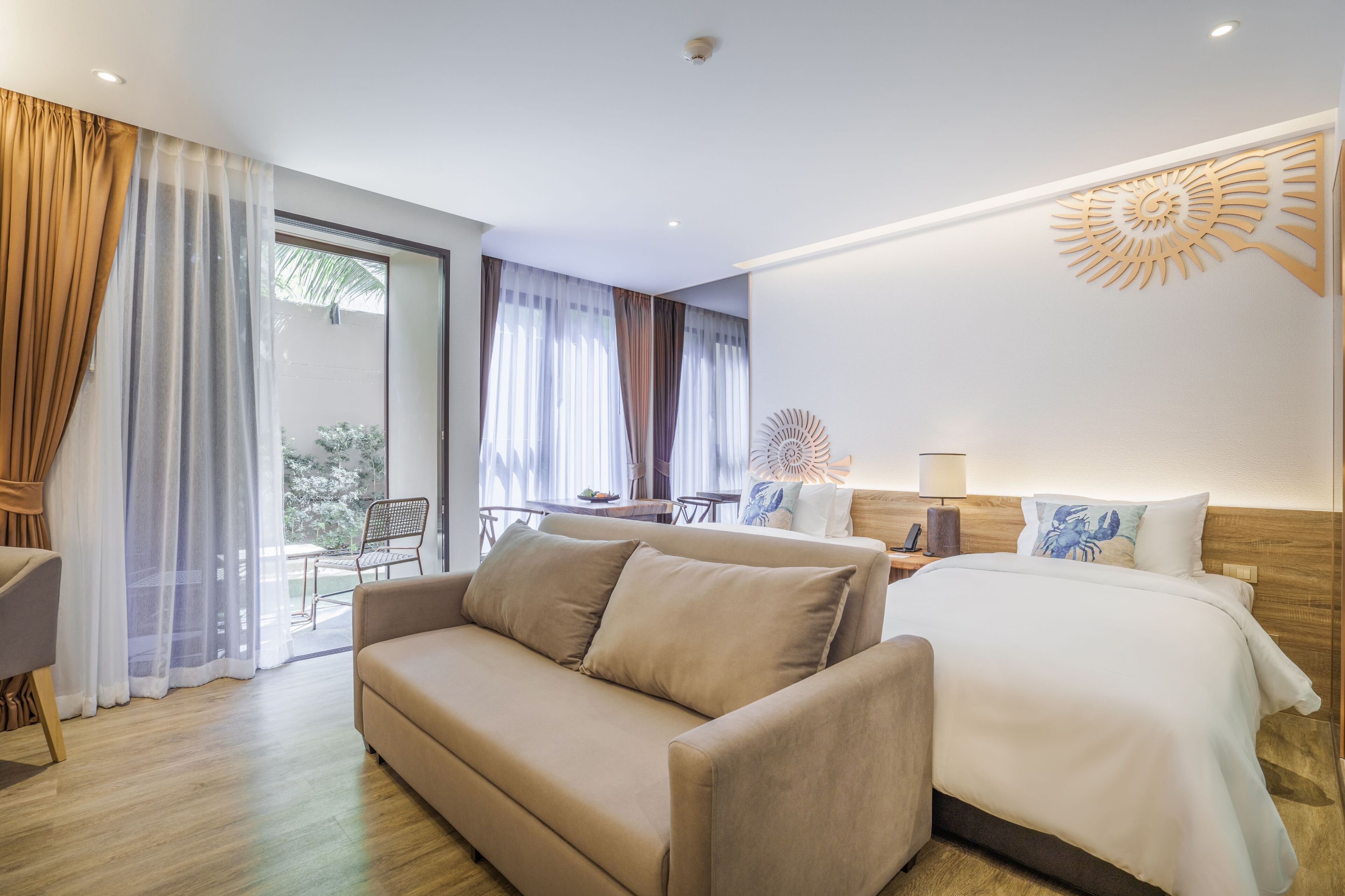 A modern hotel room with a sofa, a bed, a dining area, and a large window with curtains.