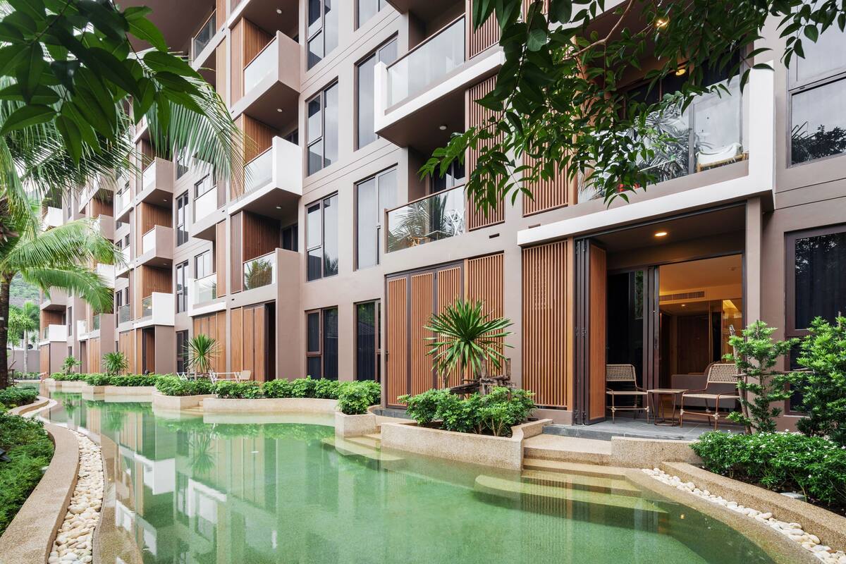 A modern hotel with a pool, balconies, and lush greenery.