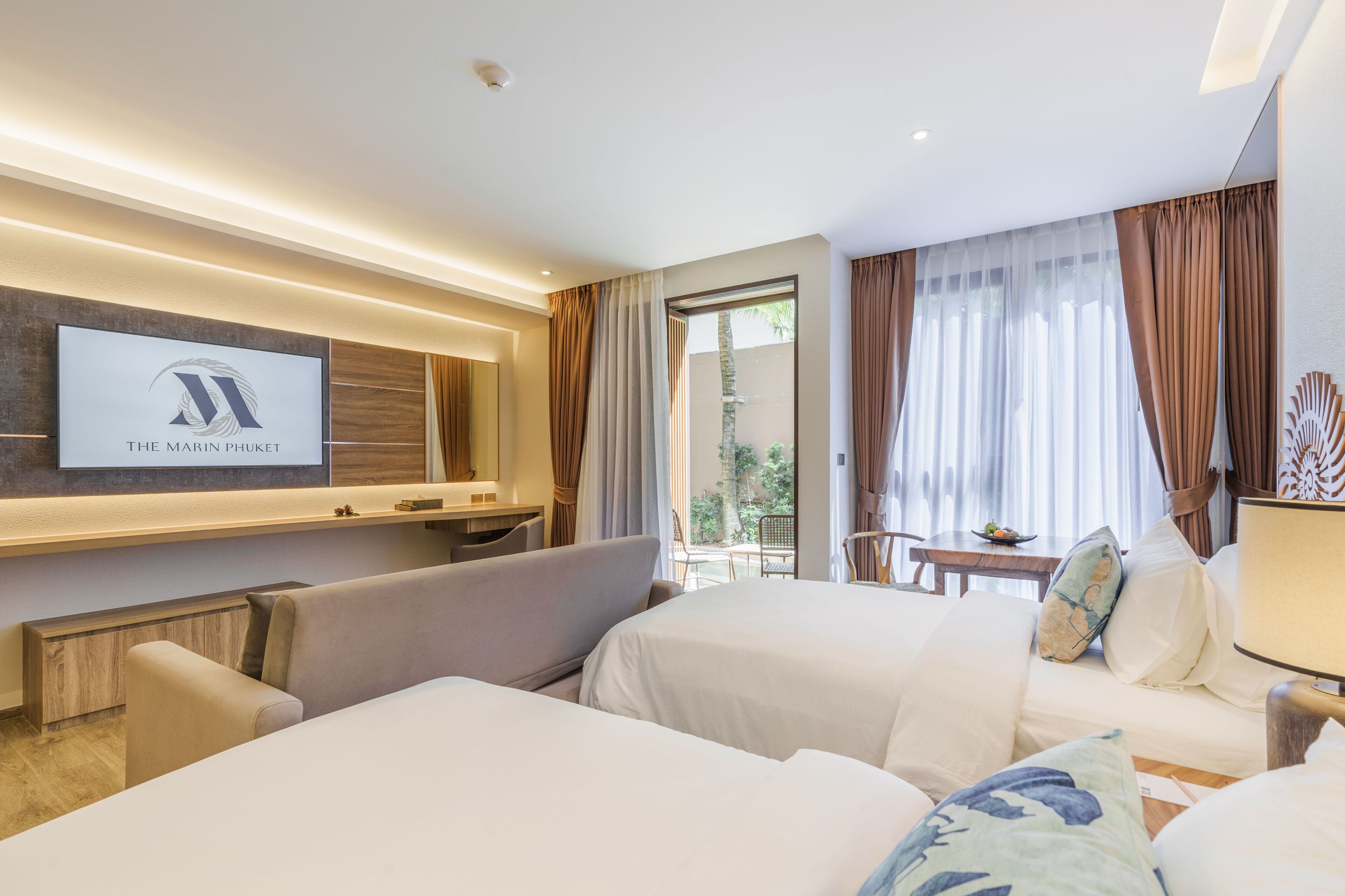 A hotel room with two beds, a TV mounted on the wall, a balcony with a table and chairs, and a view of the outdoors.