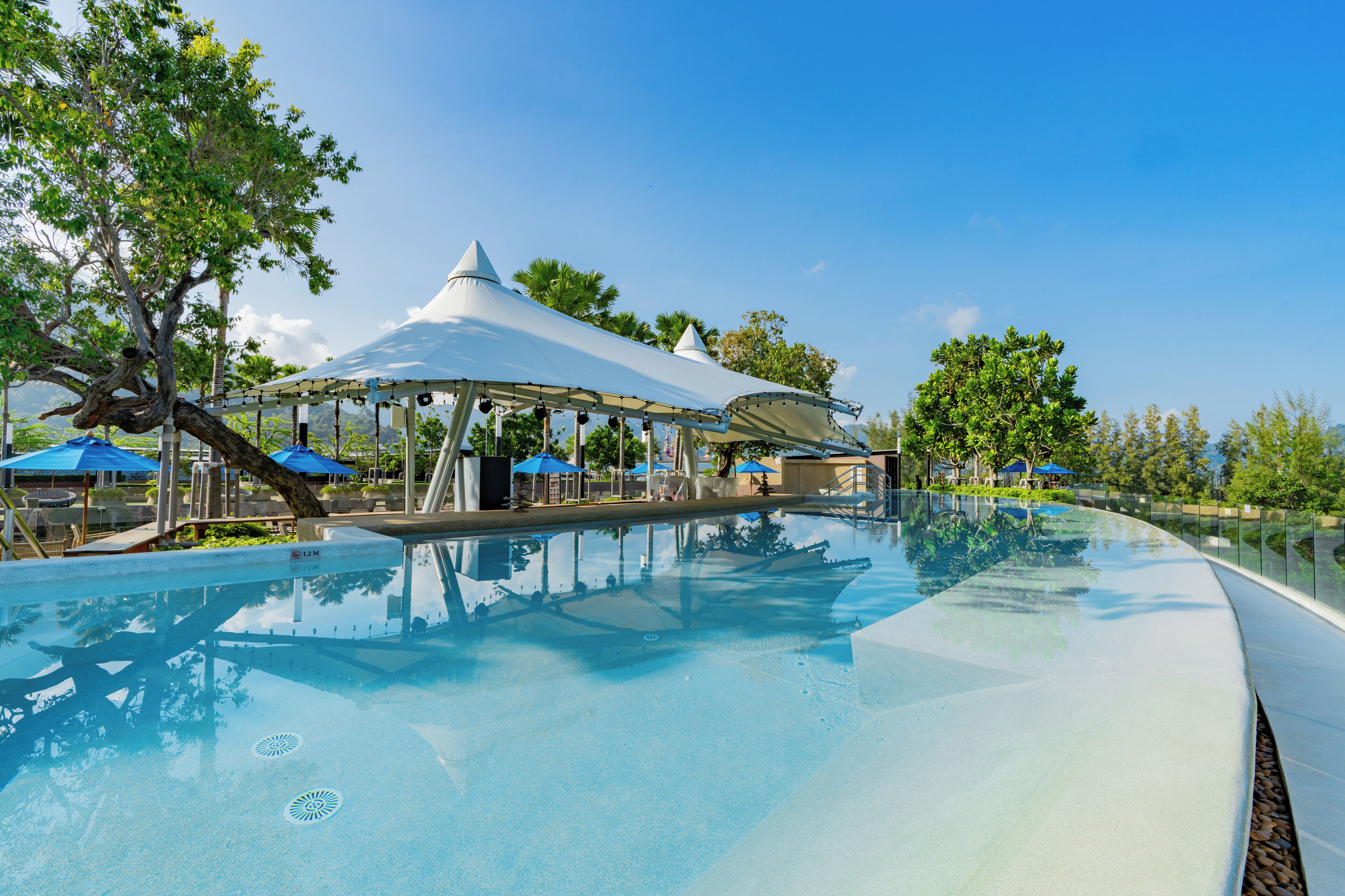 Una piscina cristalina con una marquesina blanca y sombrillas azules.