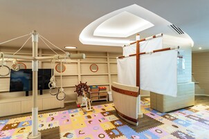 Una habitación con área de juegos, que incluye una estructura para escalar, un tapete de juego y un televisor.