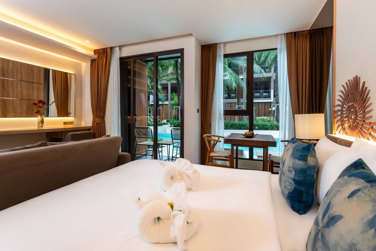 A hotel room with a large bed, a sofa, a TV, and a view of the outdoor area.