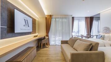 A modern hotel room with a flat-screen TV mounted on the wall, a sofa, a desk with a chair, and a dining area with a table and chairs.