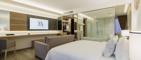A modern hotel room with a large bed, a desk, a seating area, and a large mirror.