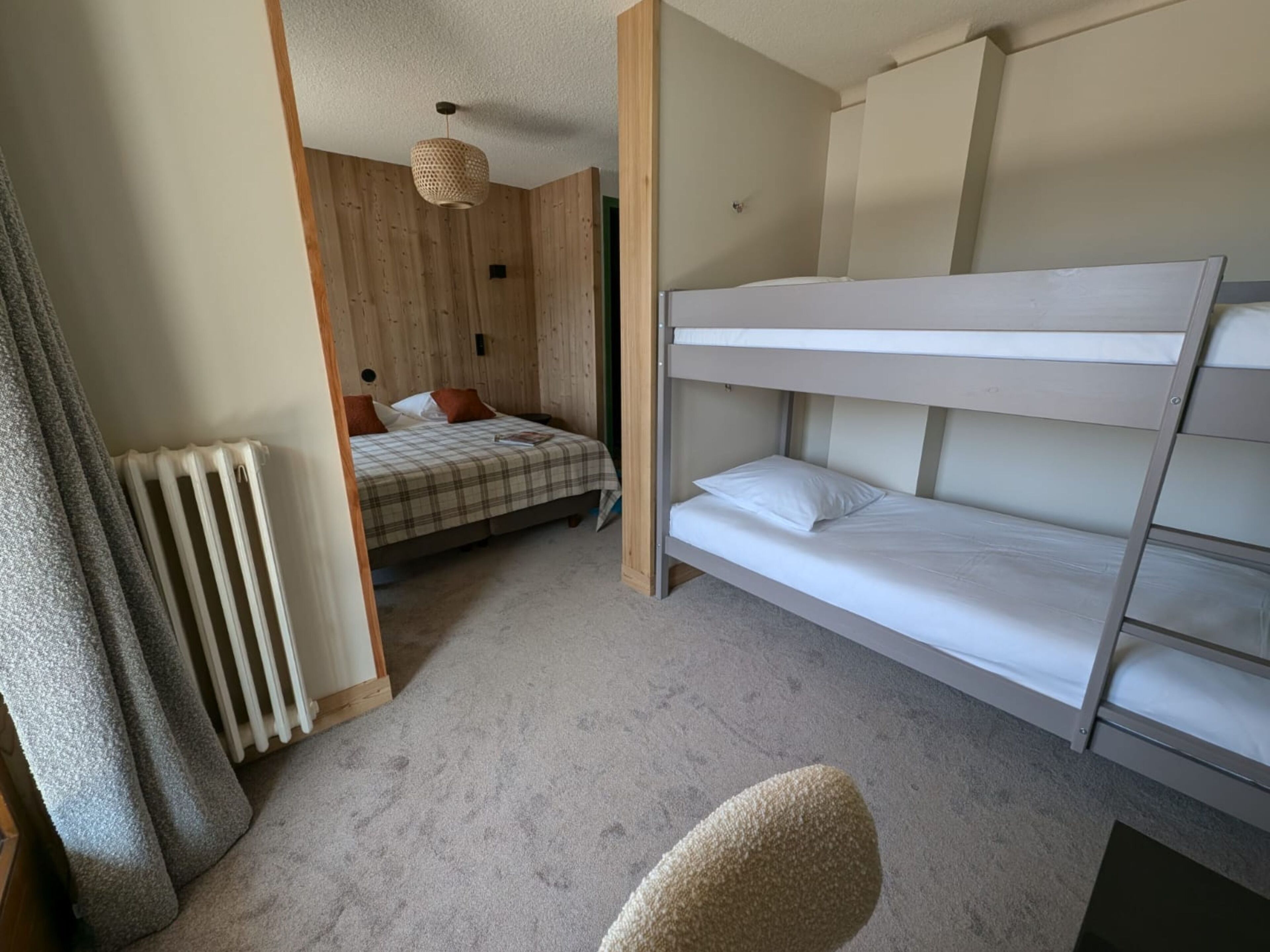 A bedroom with bunk beds, a radiator, a checkered bedspread, and a woven light fixture.