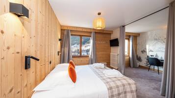 Habitación de hotel moderna con pared de madera, cama grande con ropa de cama blanca, colcha a cuadros y televisor montado. Vista a la montaña a través de la ventana.