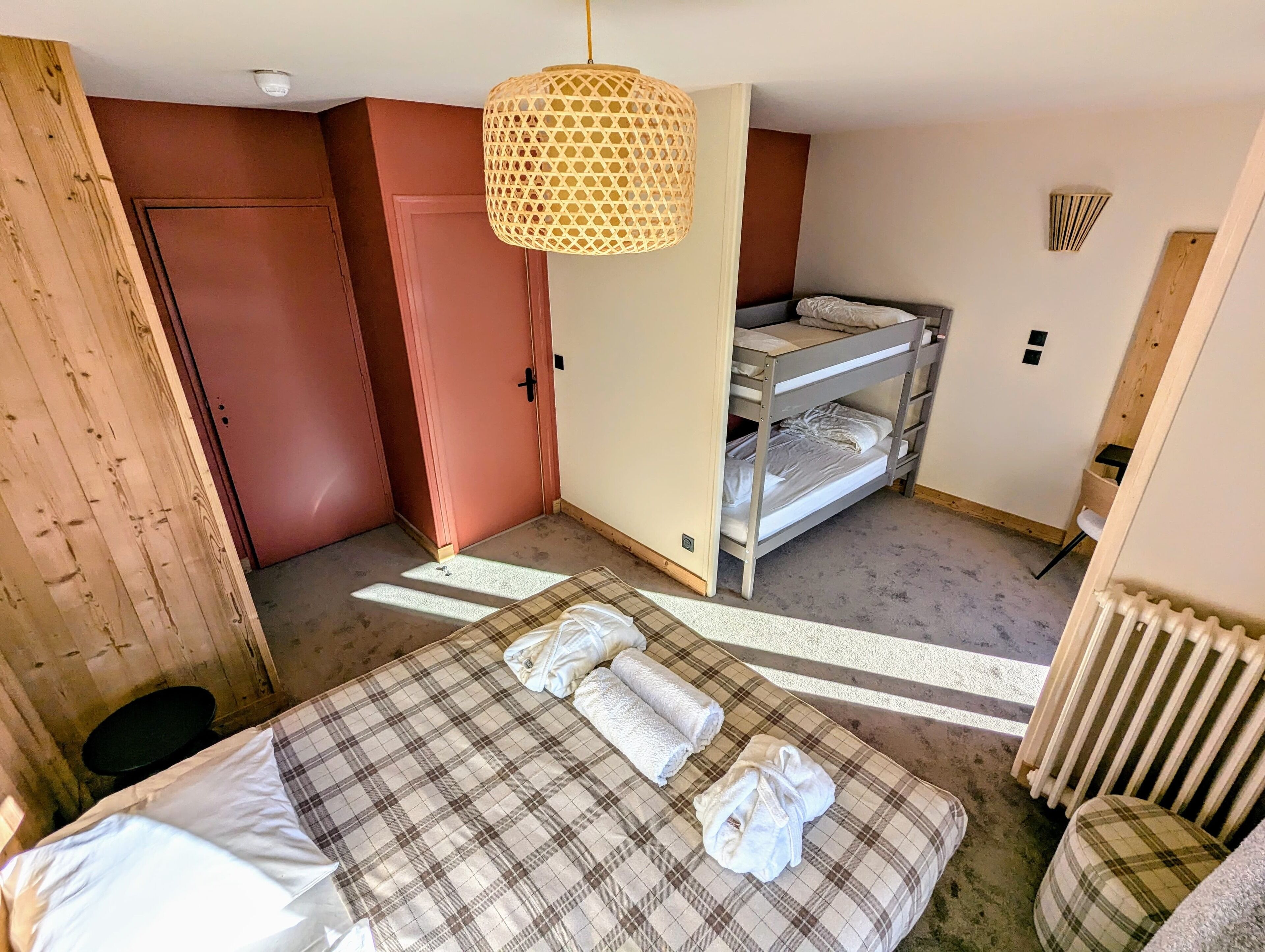 A room with a bunk bed, a bed with plaid bedding, and a hanging light fixture.