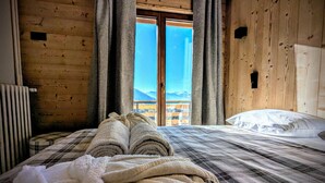 A wooden room with a bed, a radiator, and a view of mountains through a window. - Casa Moho Saint-François-Longchamp 1450 (Saint-François-Longchamp)