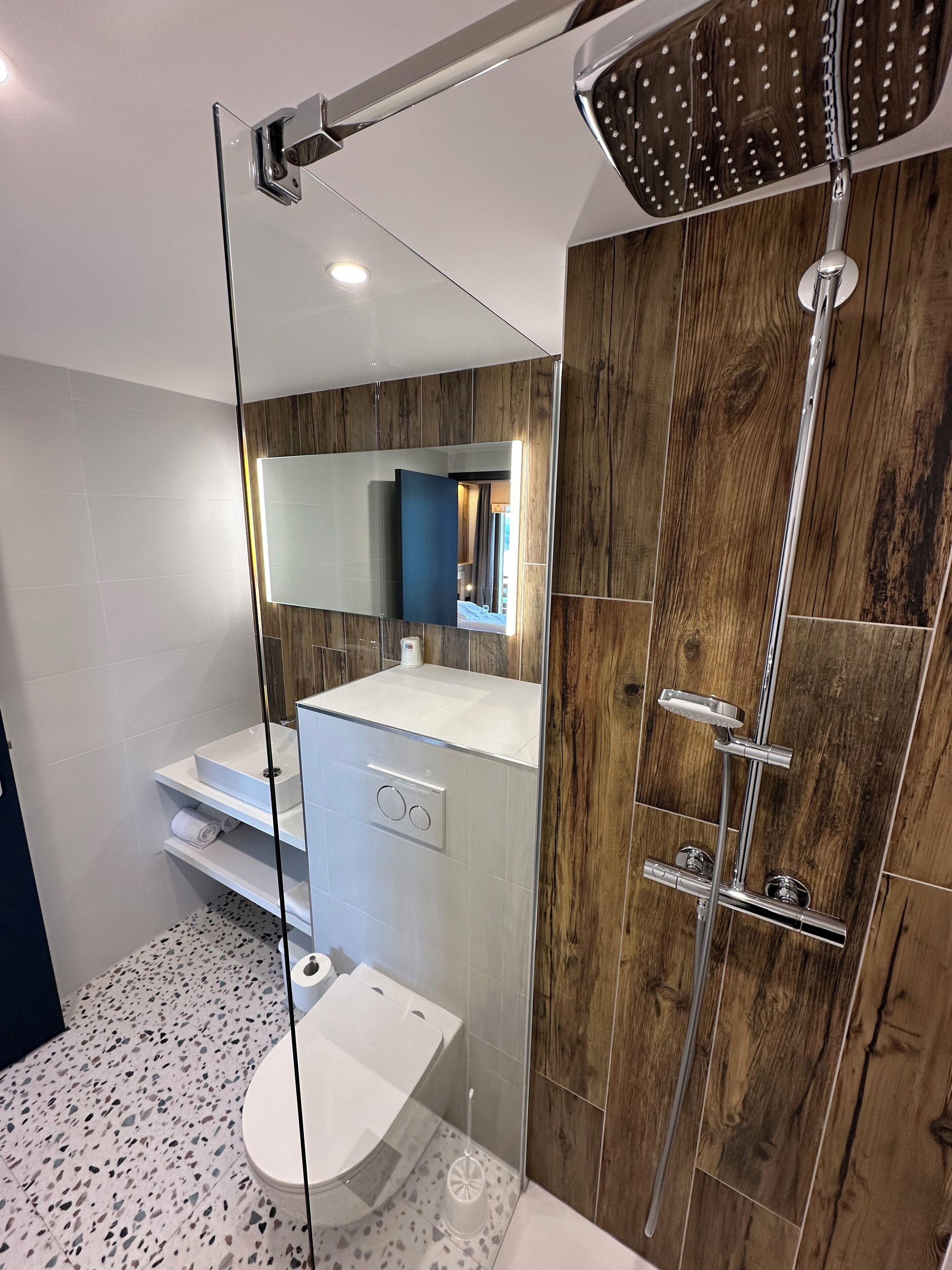 A modern bathroom with a glass-enclosed shower, a white sink, and a wooden vanity.