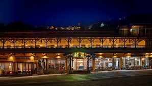 Un hotel con entrada cubierta, mesas al aire libre y una torre de reloj al fondo.