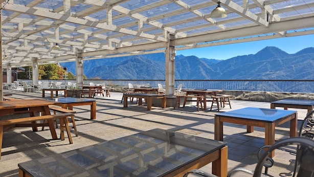 Terraza al aire libre con mesas y sillas, una estructura de pérgola y vistas a montañas.