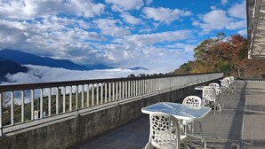 Una terraza con mesas y sillas, con vistas a un paisaje montañoso y nubes abajo.