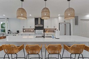 A modern kitchen with white cabinets, a central island with bar stools, and three wicker pendant lights.