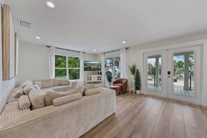 A modern living room with a large sofa, a chair, and a dining table. - Waves | Heated Pool | Steps to Beach | Golf Cart (Anna Maria)