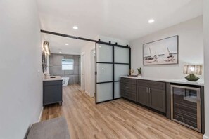 A modern kitchen with a sliding door, wooden flooring, and a painting of sailboats.