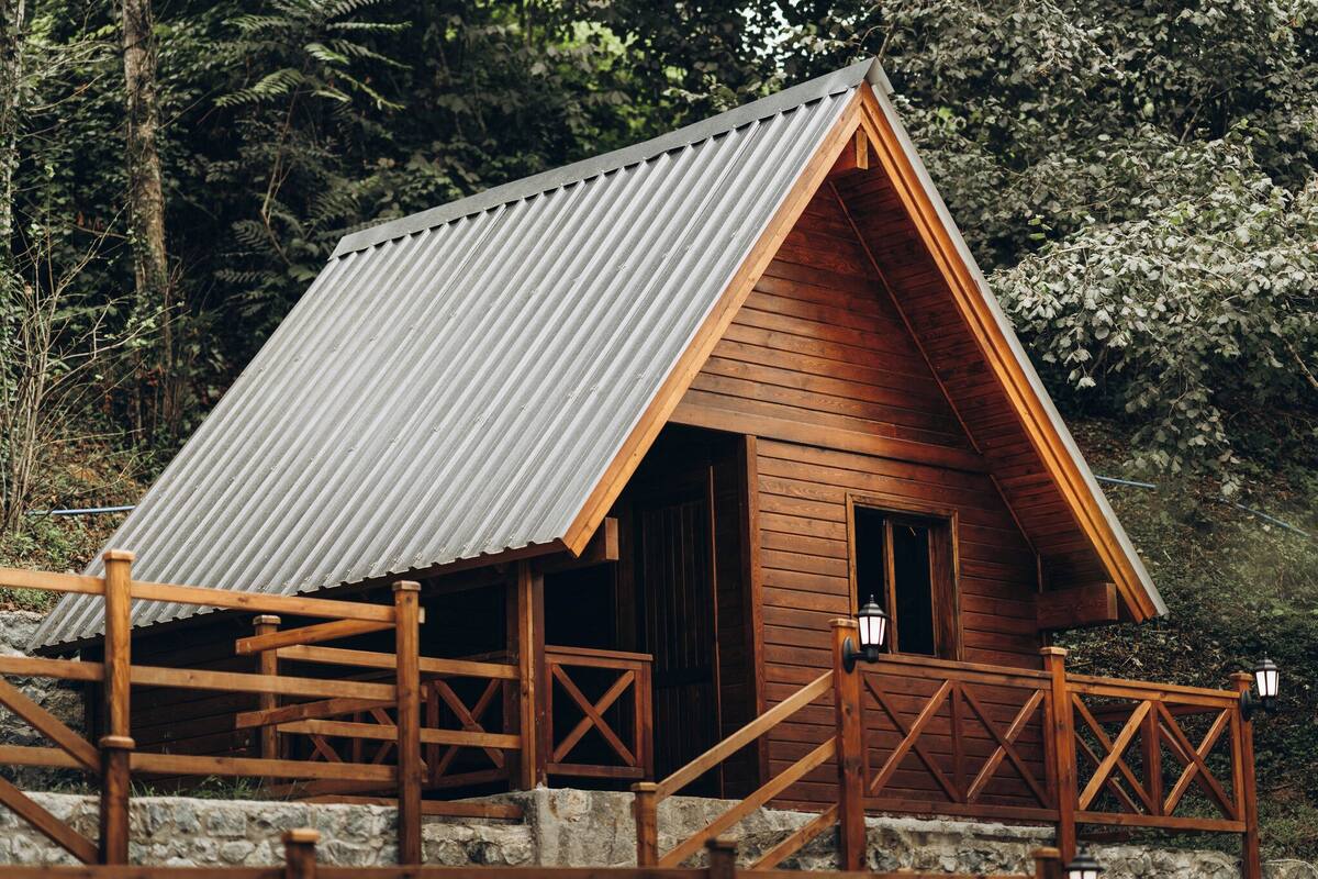 A wooden cabin with a corrugated metal roof, wooden deck, and stone steps.